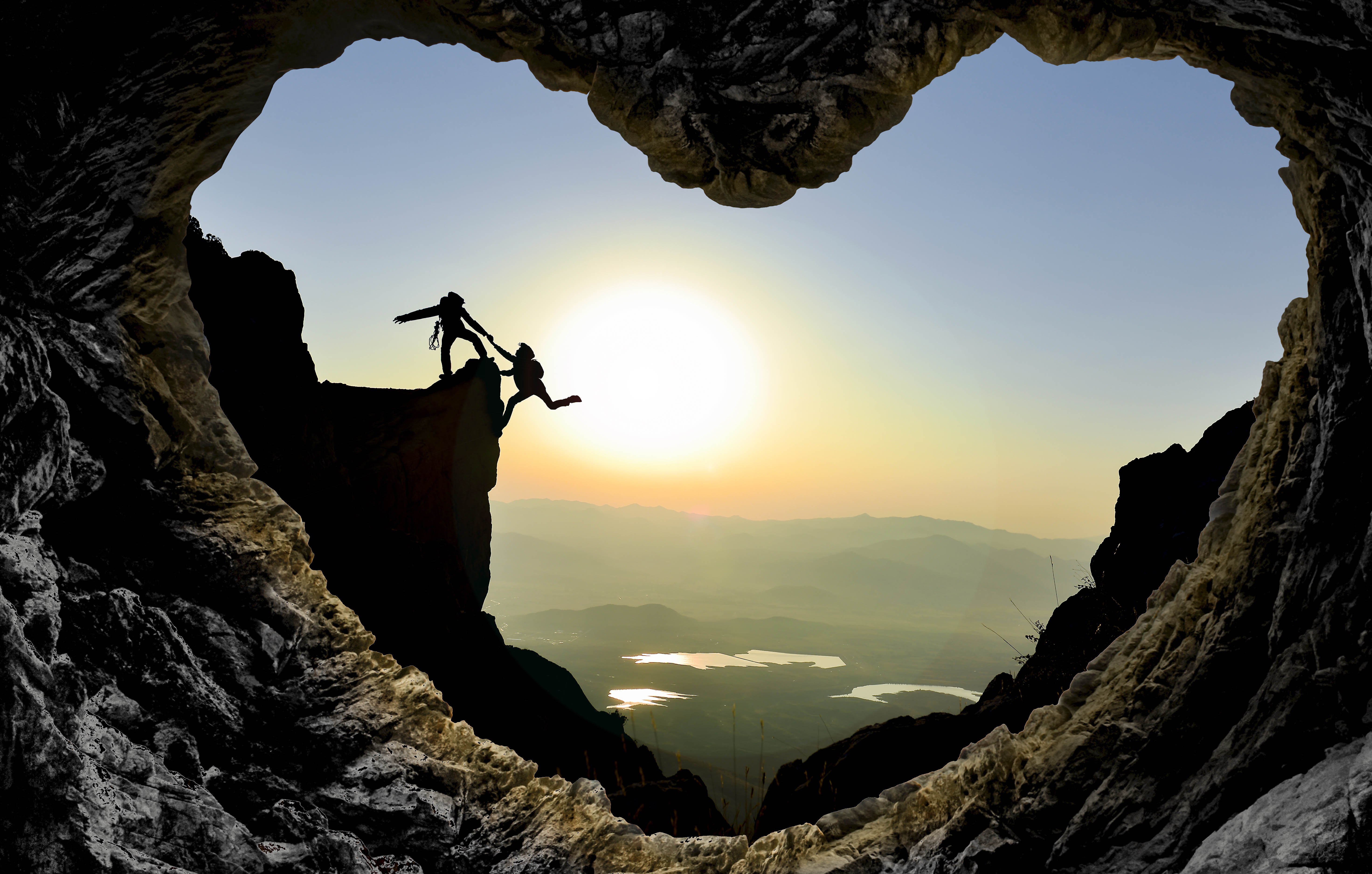 Cave in the shape of a heart, with the silhouette of two people - one helping the other up the cliff - in the twilight Cave in the shape of a heart, with the silhouette of two people - one helping the other up the cliff - in the twilight